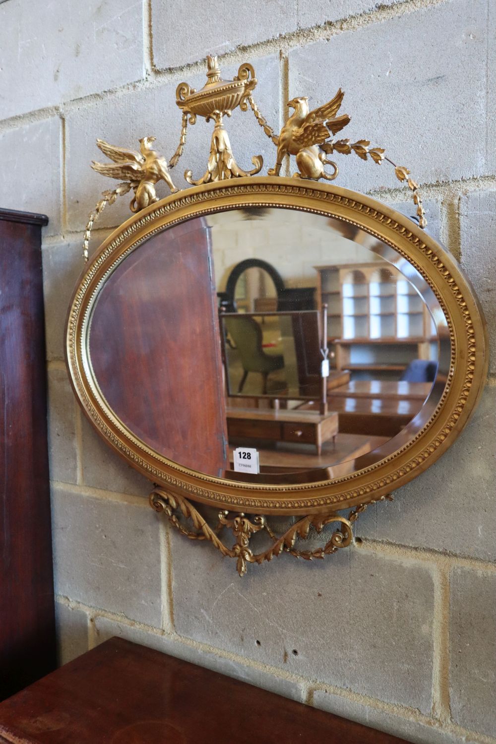 A late Victorian gilt oval wall mirror, surmounted by an urn, flanked by winged griffins, width 70cm height 75cm